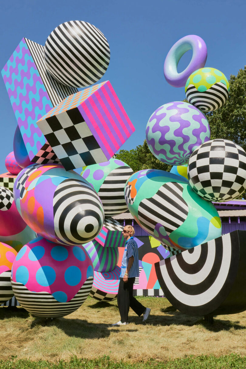 A person is among large, colorful, geometric, stripes, Polka points and check sheet models on a sunny day.