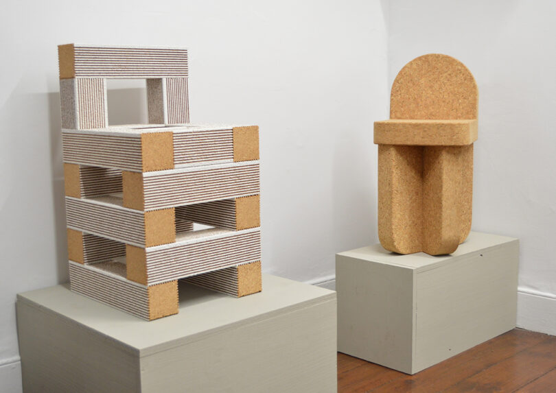 Two sculptural chairs displayed on pedestals: one is blocky with alternating striped and cork layers, the other is rounded and made of textured cork-like material.