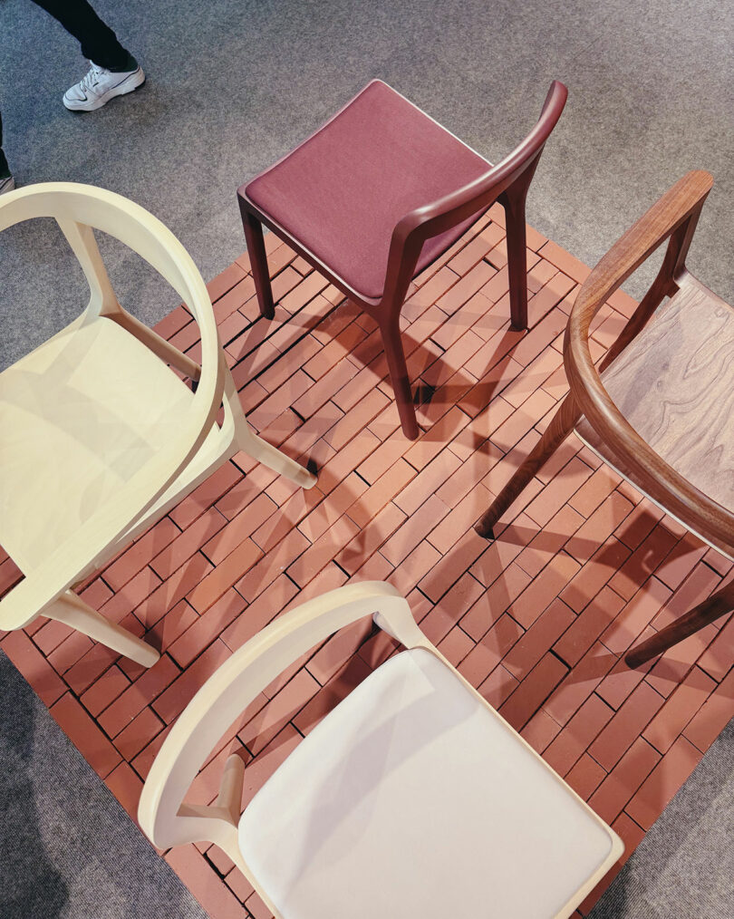 Four modern chairs of varying designs and colors are arranged on a square area of brick-patterned flooring, surrounded by carpet—an eye-catching setup.