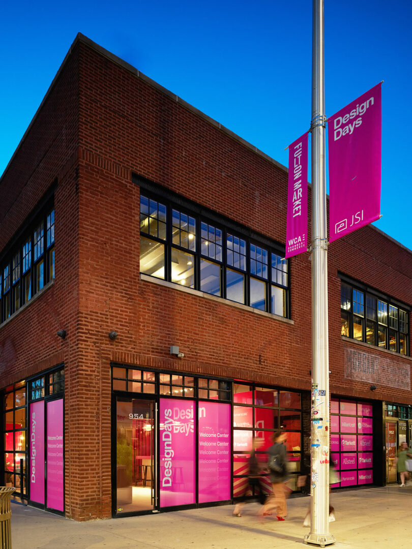 A two-story red brick building with large windows and pink banners reading "Design Days" and "JSI" stands at dusk in Fulton Market, capturing the spirit of DesignDays on its walls and streetlight.
