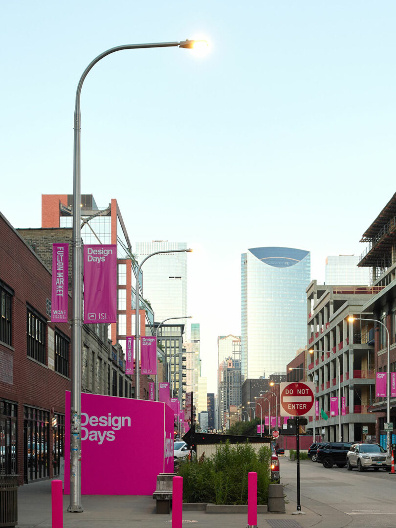 City street lined with pink "Design Days" banners and signs in vibrant Fulton Market, modern buildings in the background, and a lit streetlamp in the foreground.