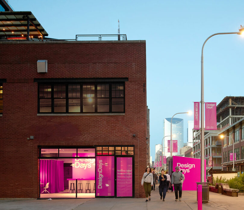 People walk past a brick building and bright pink signs for "Design Days" on Fulton Market at dusk. Banners and posters advertise the DesignDays event throughout the area.