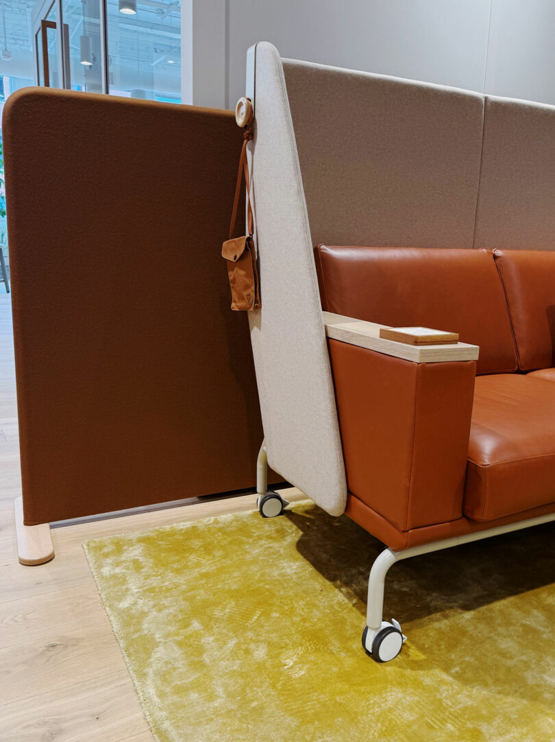 Brown and beige partition next to a brown leather sofa on wheels, with a small brown bag hanging on the divider, set on a yellow rug in a modern room at Fulton Market DesignDays.