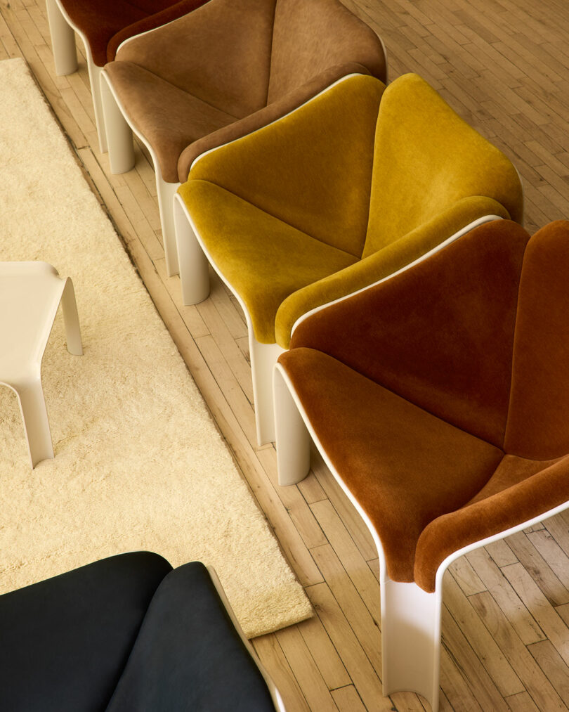 A modern lounge featuring F300 Pierre Paulin curved chairs in warm colors, low white tables, a cream rug, wood cabinetry, speakers, and a pendant light in a minimalist setting.
