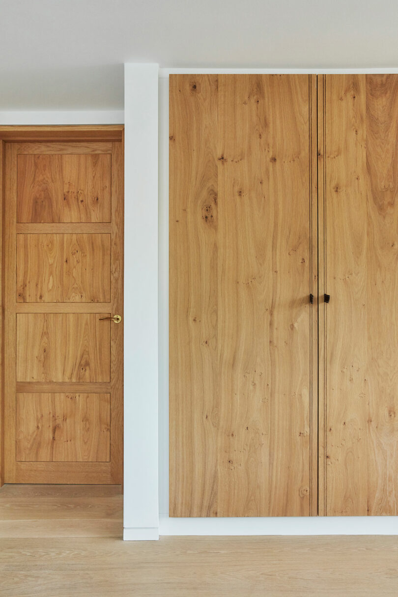 A wooden door and a built-in wooden wardrobe with simple black handles, set against white walls and a light wood floor.