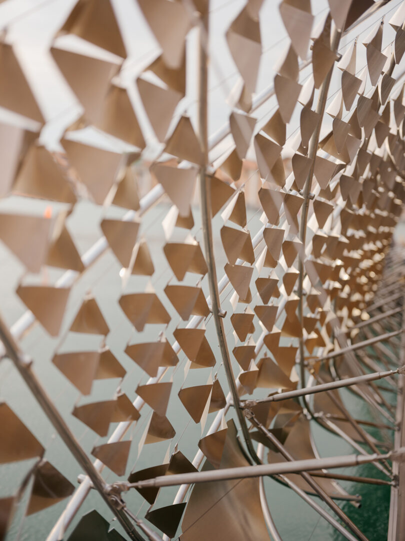 Close-up of a metal structure with repeating triangular shapes, arranged in a geometric pattern, reflecting sunlight.
