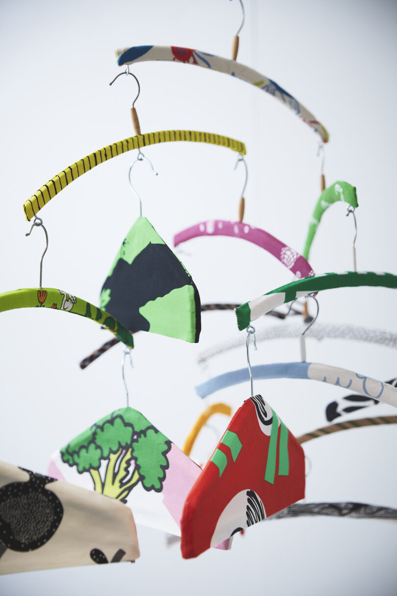 Several clothing hangers covered in colorful, patterned fabric hang suspended in mid-air against a plain background.