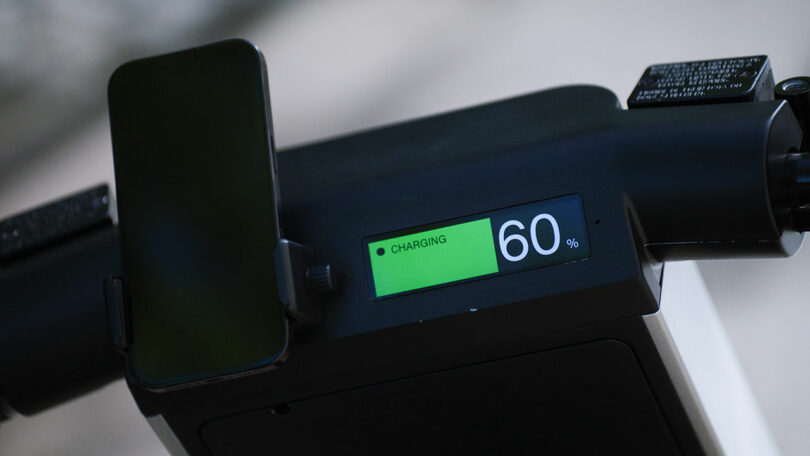 Close-up of an electronic device display showing "CHARGING 60%" with a smartphone placed in a holder on the left side.