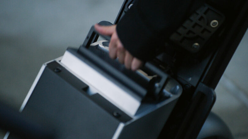 A close-up of a hand lifting a handle on a rectangular device with a metallic finish and a control panel beside it.
