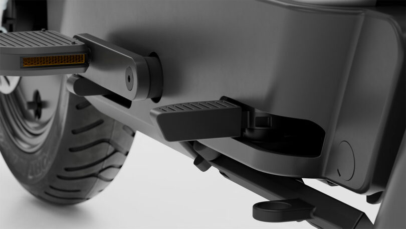 Close-up view of a vehicle's rear section showing a tire, a footrest, a step, and suspension components in a matte black finish.