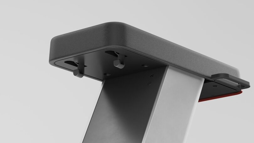 Close-up view of a modern, rectangular metal and plastic structure with two protruding black hooks, set against a plain gray background.
