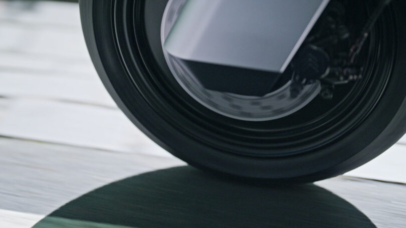 Close-up of a black motorcycle or bicycle wheel in motion, with its shadow visible on a paved surface.