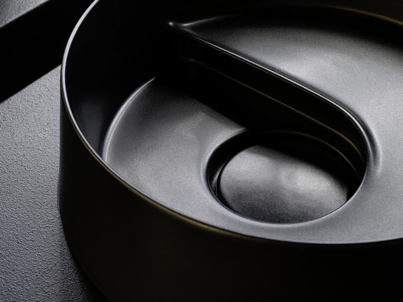 Close-up of a black, round, segmented tray or container with a textured surface and a curved central divider.