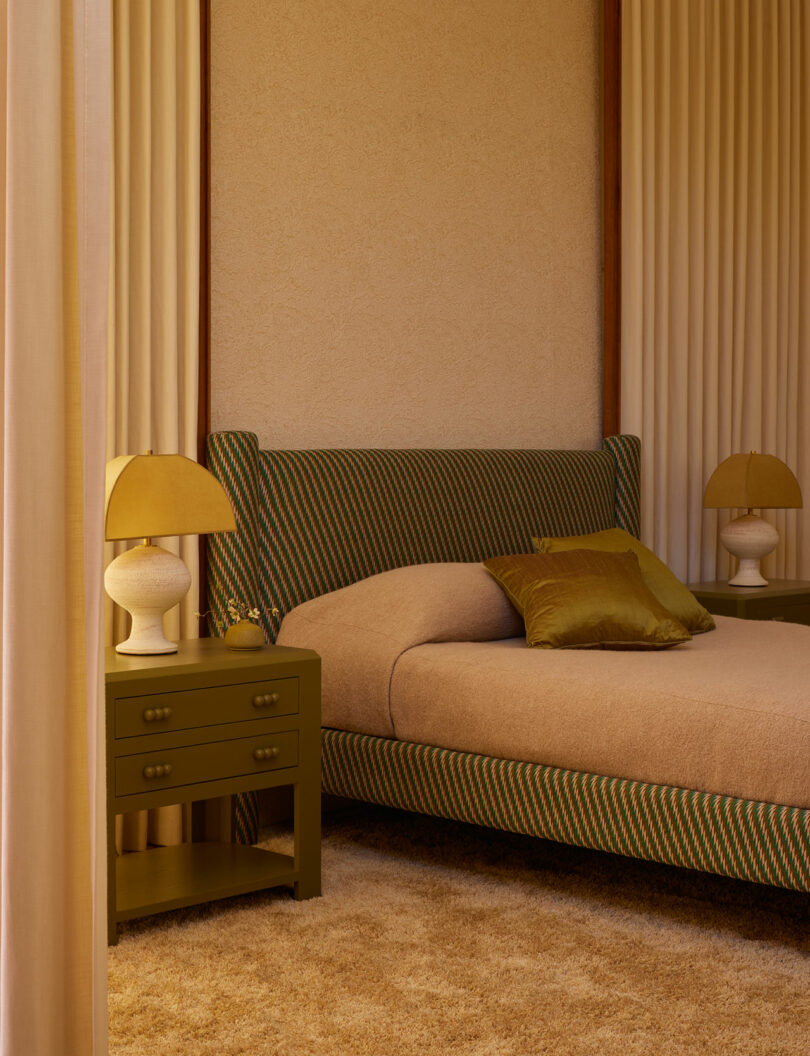 A bedroom from the Agapanthus Collection featuring a striped upholstered bed, beige bedding, green side tables, matching lamps, and floor-to-ceiling curtains.