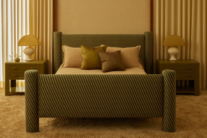 A bedroom from the Agapanthus Collection features a striped green upholstered bed, beige bedding, two green nightstands with lamps, and floor-length curtains on both sides.