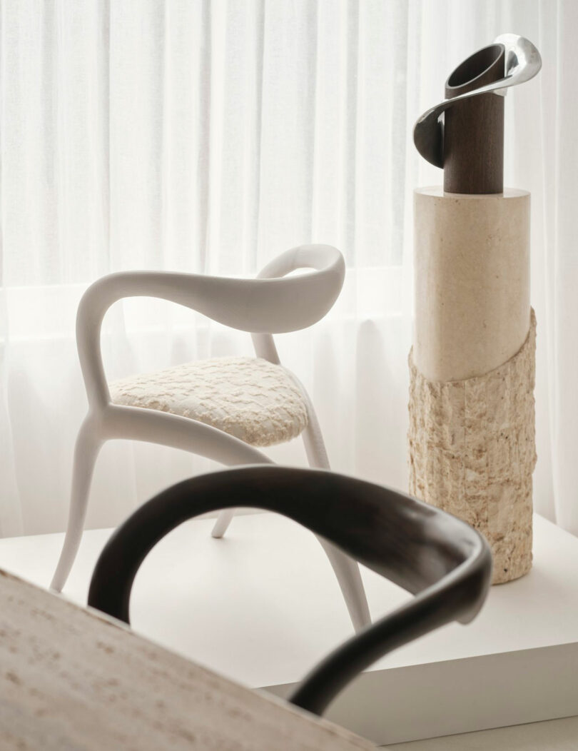 Modern Miminat minimalist room featuring a sculptural white chair with a textured seat and an abstract metal and stone sculpture, set against sheer white curtains.