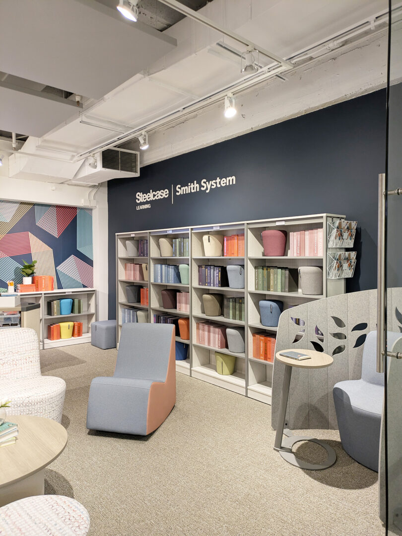 A modern library room with bookshelves, colorful books, seating options, decorative partitions, and a wall labeled "Steelcase Smith System"—a NeoCon 2025 Top 10 design highlight.