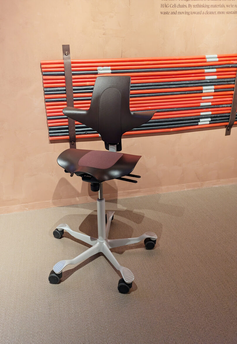 A black ergonomic office chair on a gray carpet, positioned in front of a wall with bundled red and black rods mounted horizontally.