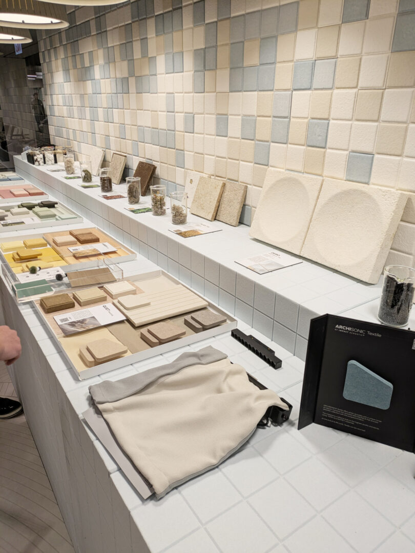 Samples of tiles and building materials are displayed on a tiled counter with informational cards and fabric swatches in a showroom setting.