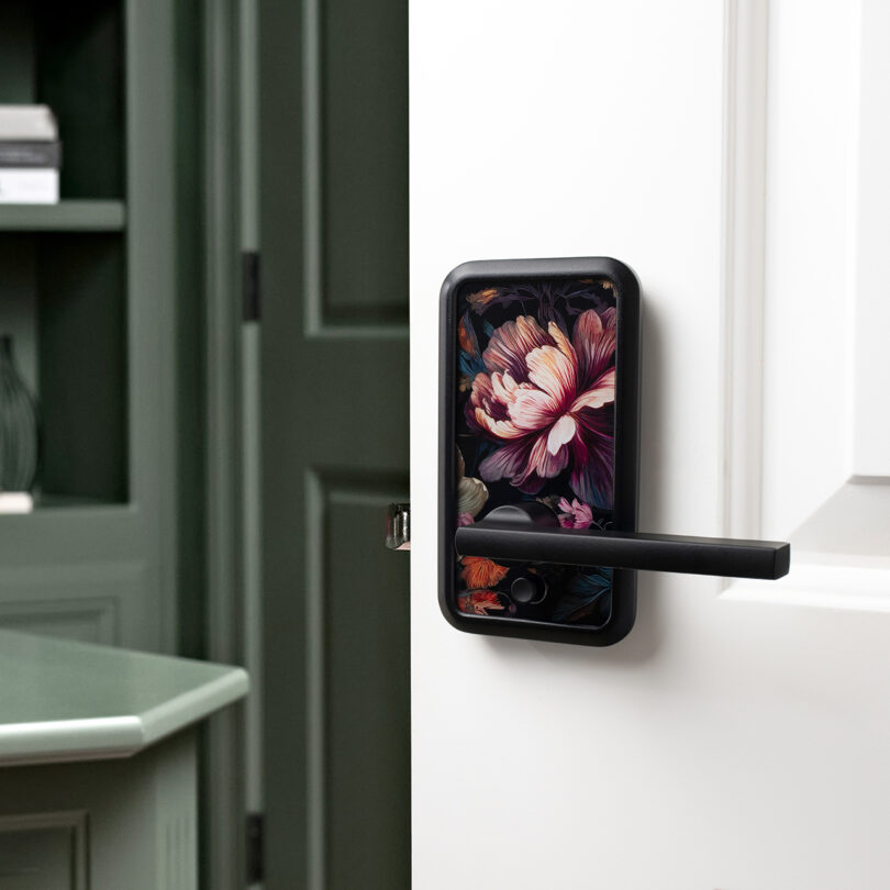 A black door handle with a floral design is installed on a white door, partially open, with green cabinetry visible in the background.