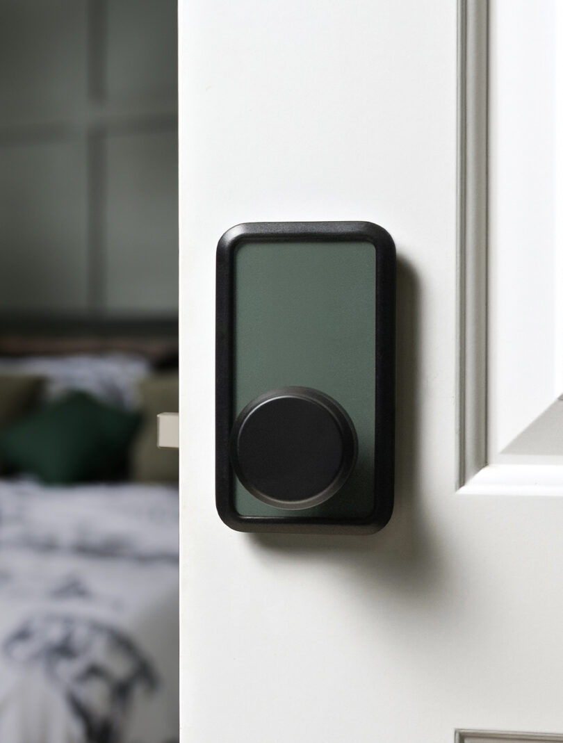 A black and green modern smart door lock is installed on a white door, partially open to reveal a blurred bedroom interior.