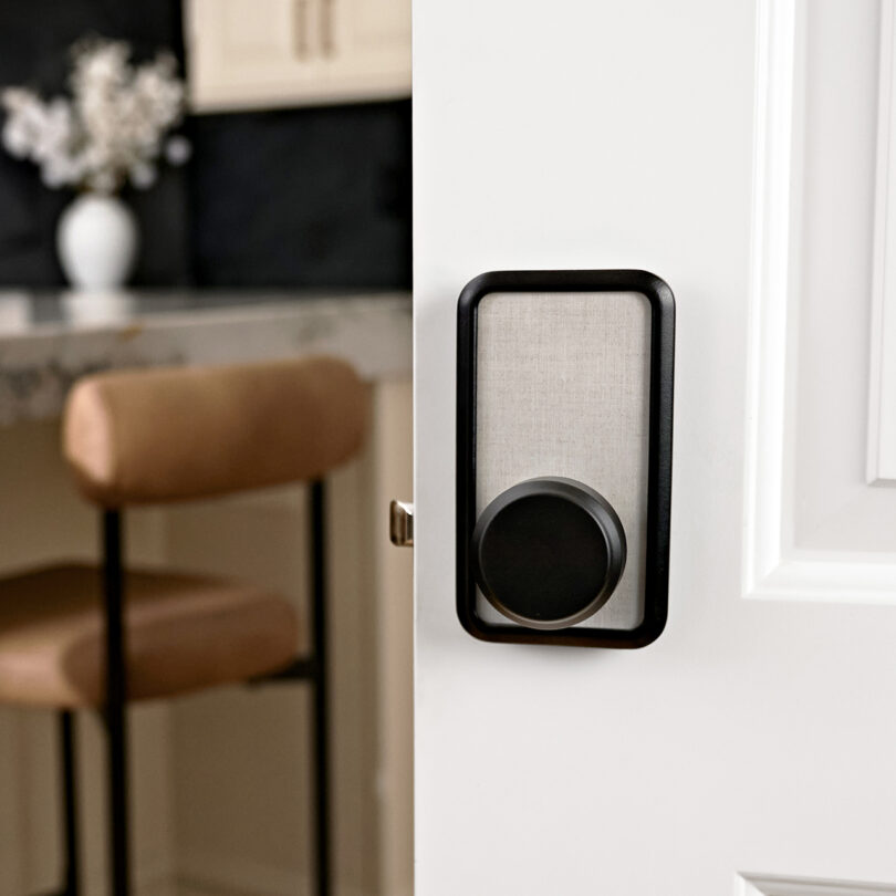 A linen print modern smart door lock is installed on a white door, partially open to reveal a blurred kitchen interior.