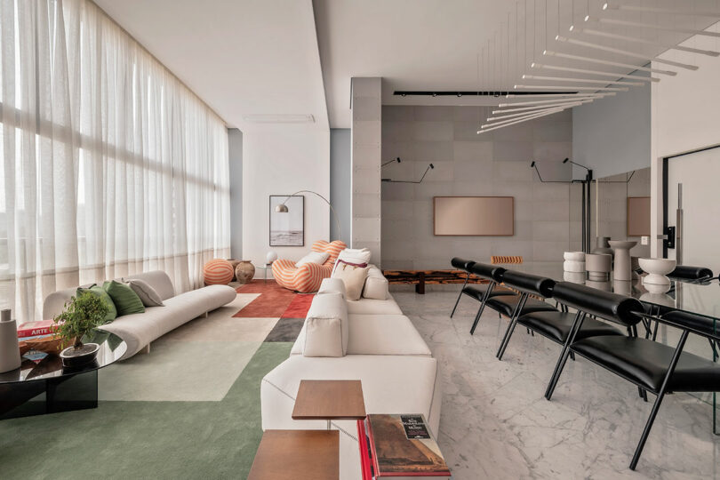 Modern living room with marble floors, minimalist white sofas, black chairs, geometric rugs, striped accent chairs, and floor-to-ceiling windows with sheer curtains.