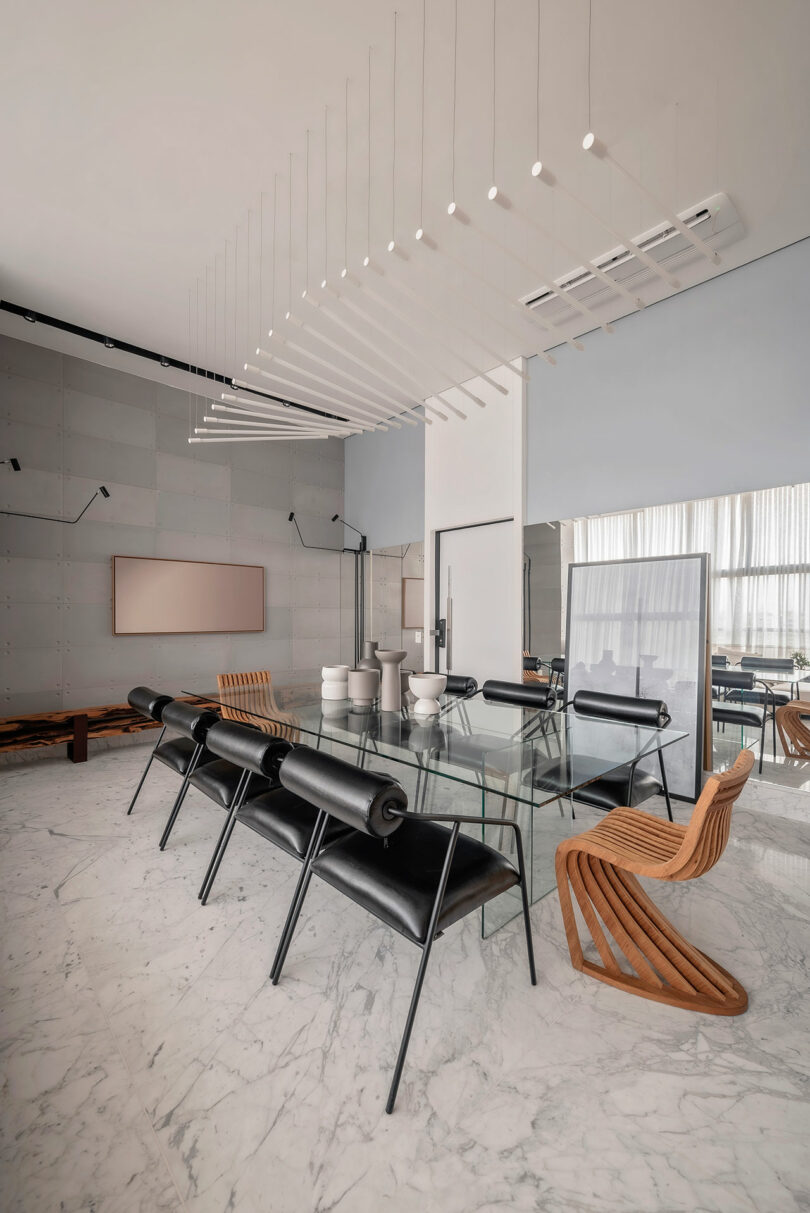 Modern dining room with a glass table, black and wooden chairs, marble floor, wall-mounted TV, and a geometric ceiling light fixture.