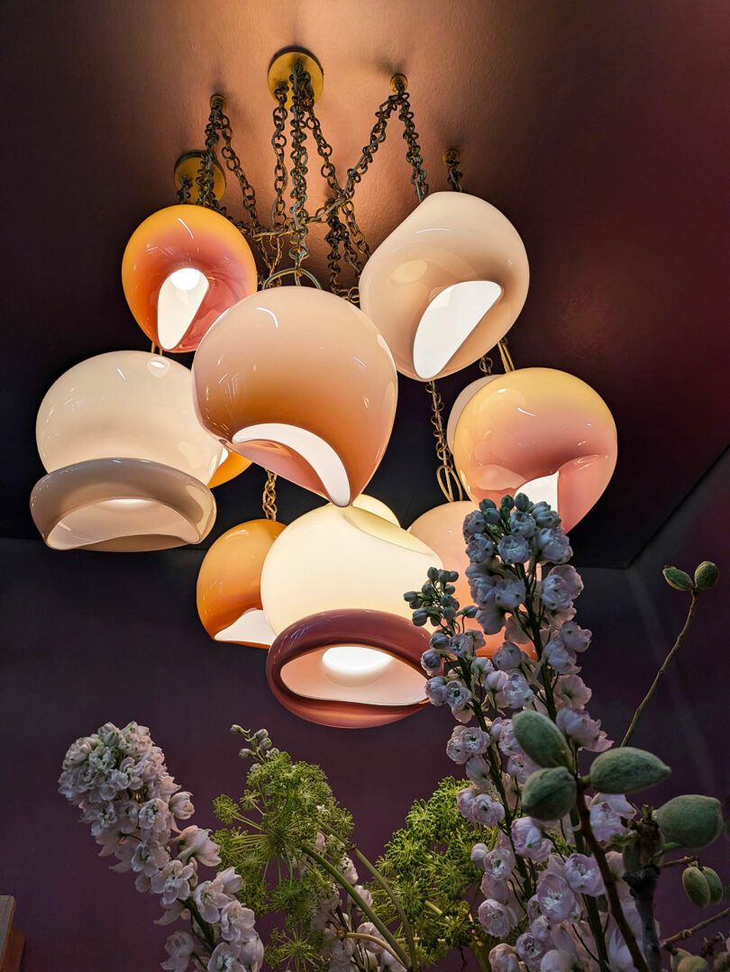 A cluster of modern pendant lights with round, white and peach glass shades hangs from the ceiling above floral arrangements, creating a stylish ambiance.