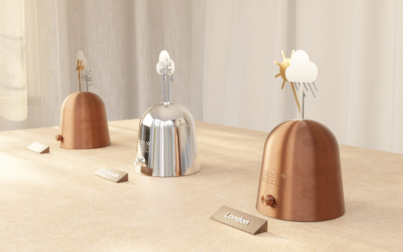 Three dome-shaped weather devices labeled London, Stockholm, and another city display weather symbols on top, placed on a beige surface with a light curtain backdrop.