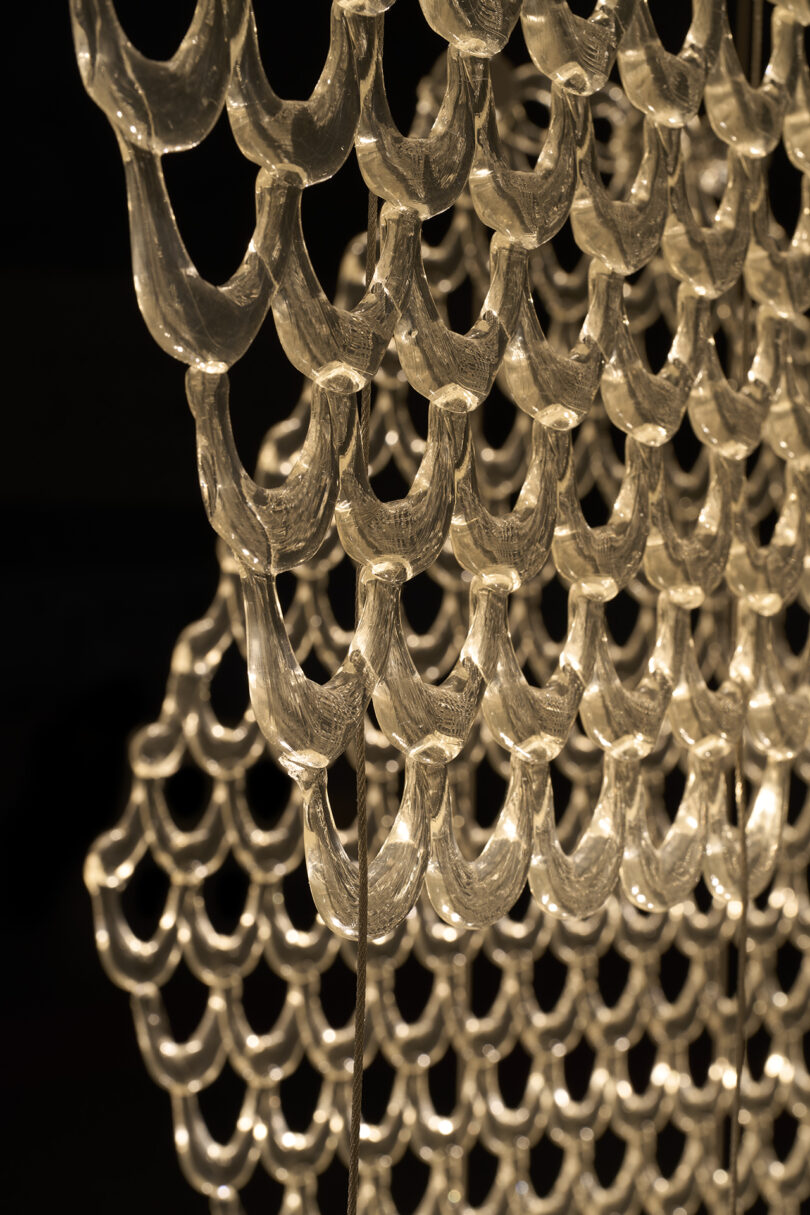 A close-up view of a decorative glass chandelier with multiple curved, interlocking elements illuminated by warm light, reminiscent of the branches of The Great Tree.