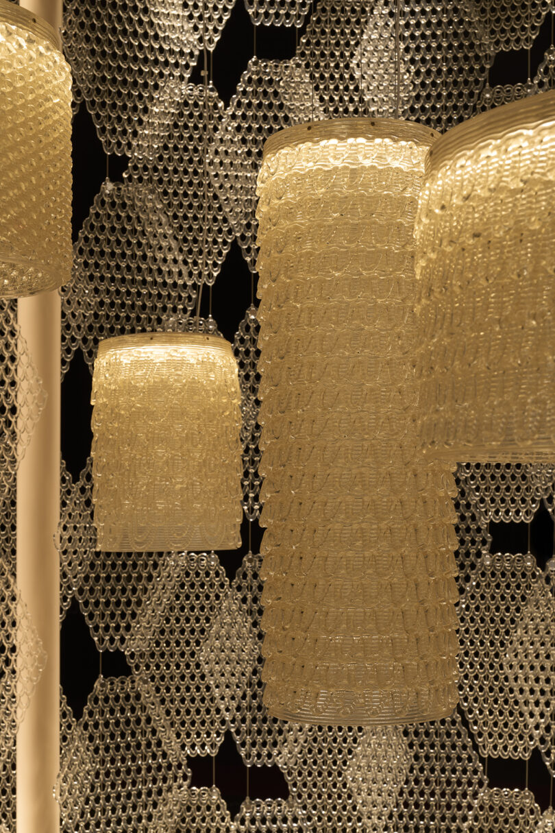 Multiple cylindrical pendant lamps with textured, translucent surfaces hang in front of a geometric, honeycomb-patterned background reminiscent of The Great Tree’s intricate beauty.