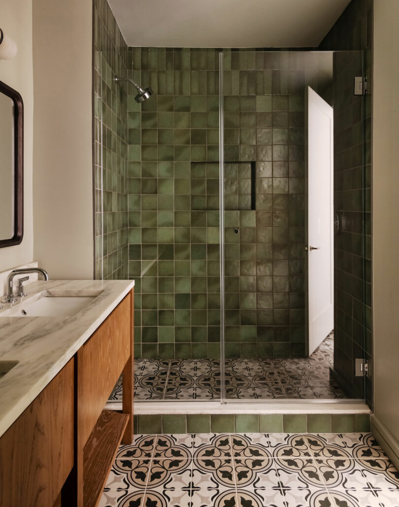 Bathroom with a glass-enclosed shower featuring green square tiles, a marble countertop vanity with wood cabinetry, and patterned floor tiles.