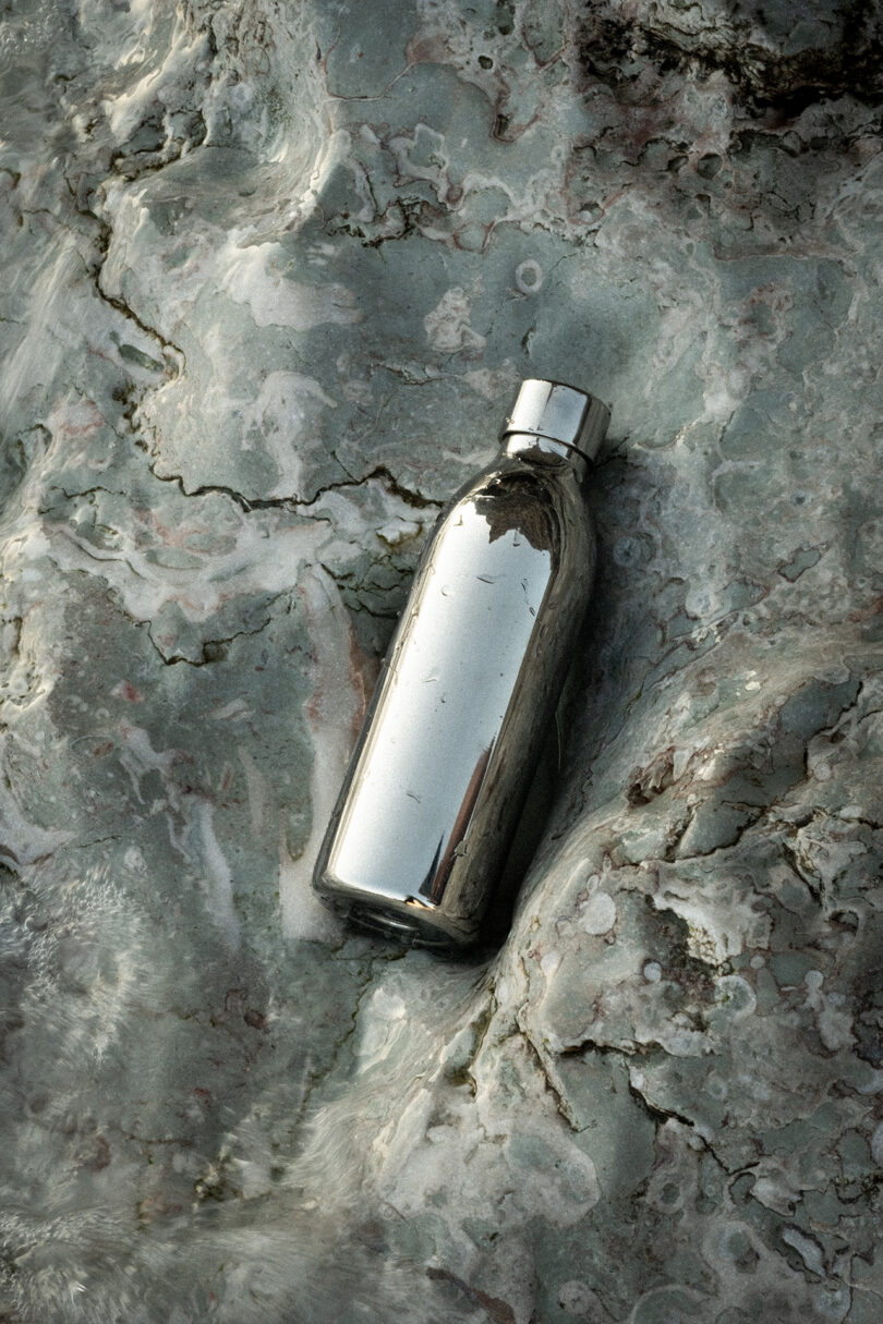 An Aarke To-Go Bottle made of stainless steel lies on a textured, gray stone surface.