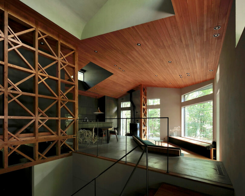 Modern interior with wooden ceiling and lattice divider, open kitchen, large windows, and natural light illuminating a split-level living space with minimalist furnishings.