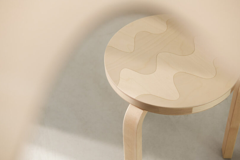 A light wood stool with a round seat featuring an interlocking wavy pattern, photographed from above on a light-colored floor