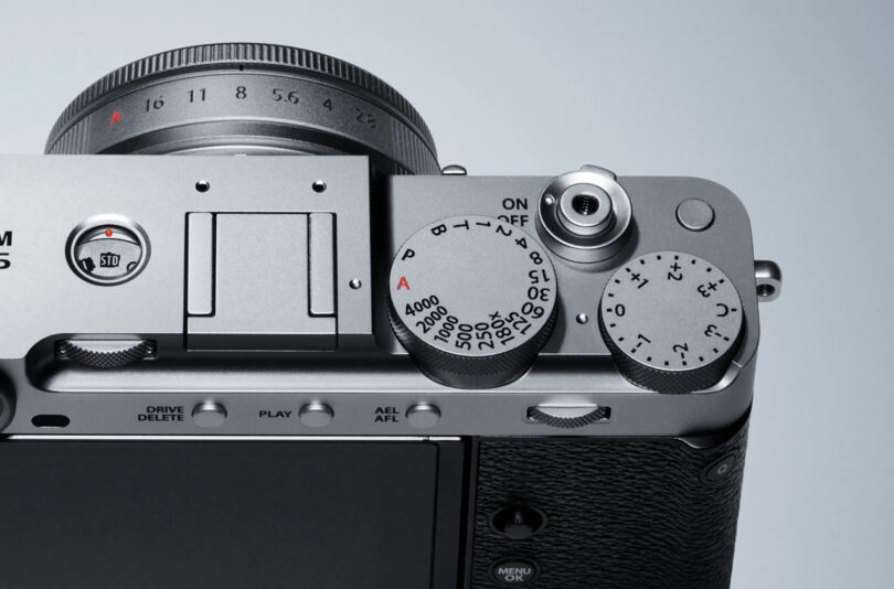 Close-up view of a Fujifilm X-E5 digital camera's top controls, showing dials for shutter speed, exposure compensation, and the power switch surrounding the shutter button.