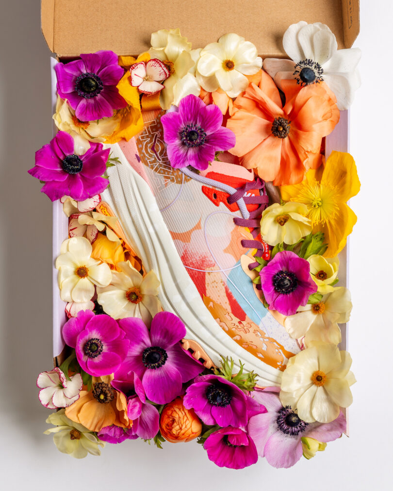 A pair of colorful sneakers in a box surrounded by an arrangement of vibrant artificial flowers in various colors