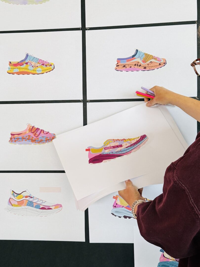 A person holds a sneaker illustration while arranging colorful sneaker drawings on a wall display grid