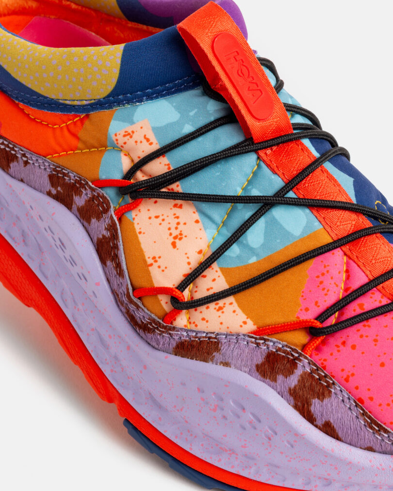 Close-up of a multicolored sneaker with abstract patterns, black laces, a red tongue, and a speckled purple sole
