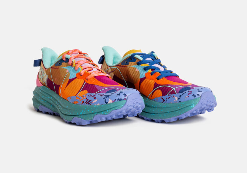 A pair of colorful athletic shoes with mismatched laces, featuring orange, purple, teal, and blue accents on a chunky lavender sole