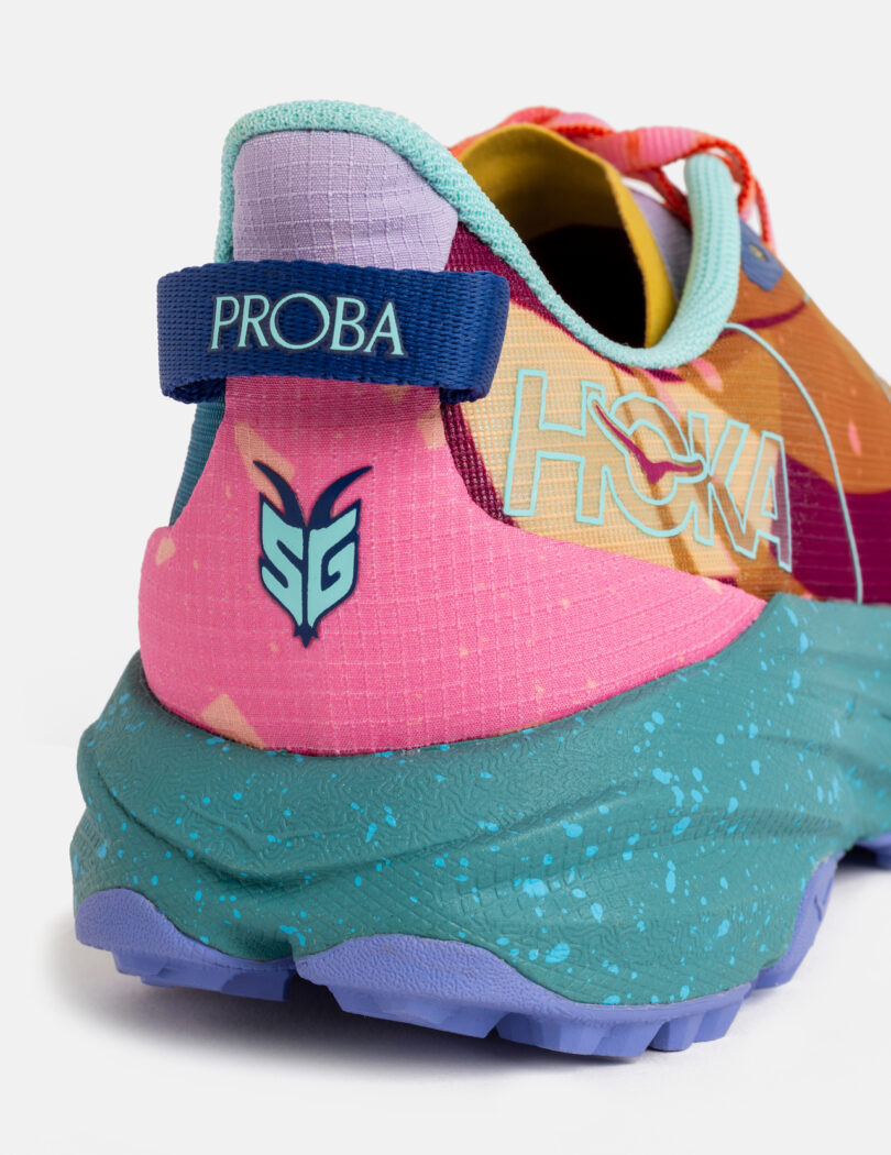 Close-up of the heel of a multicolored HOKA running shoe with "PROBA" on the pull tab and a stylized logo above the speckled blue sole