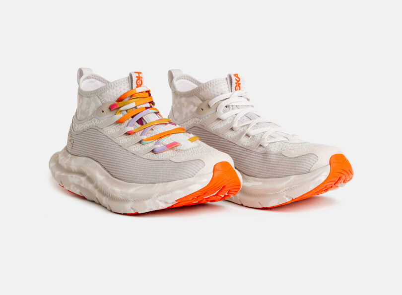 A pair of white athletic sneakers with chunky soles and orange accents; one shoe has multicolored laces, the other has plain white laces