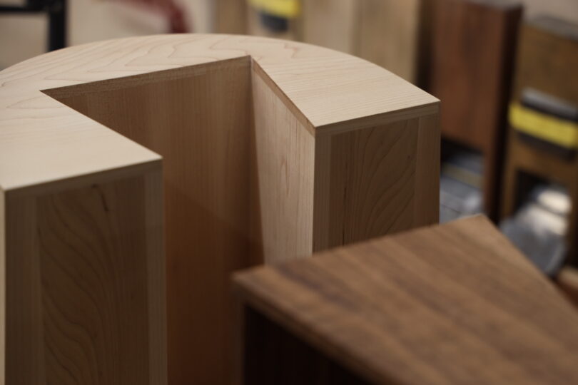 Close-up of a wooden structure with a large V-shaped notch, surrounded by other wooden objects in a workshop setting