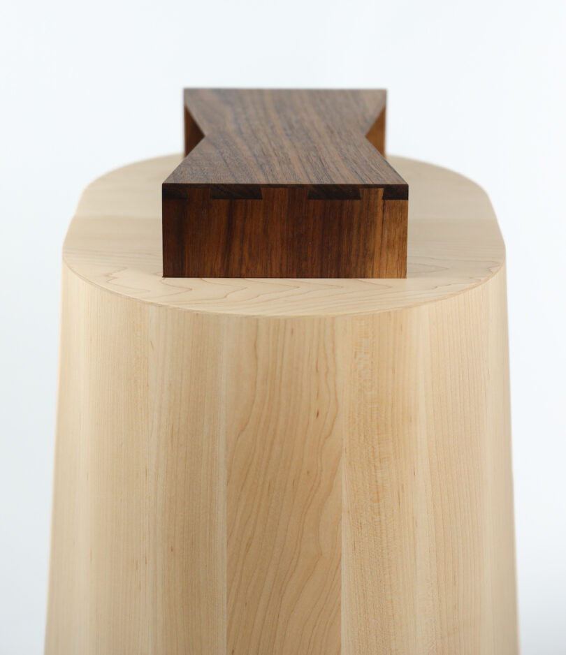 Oval wooden stool with a contrasting dark wood bowtie-shaped inlay