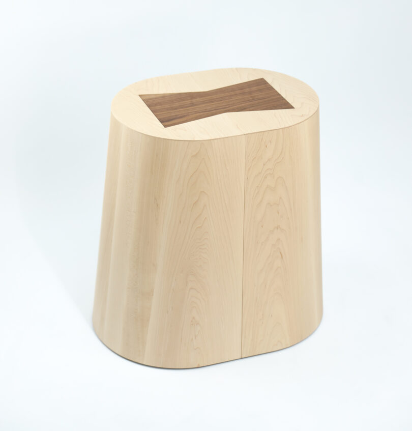 Oval wooden stool with a contrasting dark wood bowtie-shaped inlay