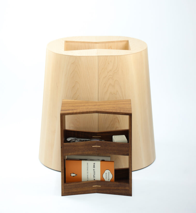 A wooden stool with a hollow center, accompanied by an open wooden box containing a book and several small items, all set against a plain white background