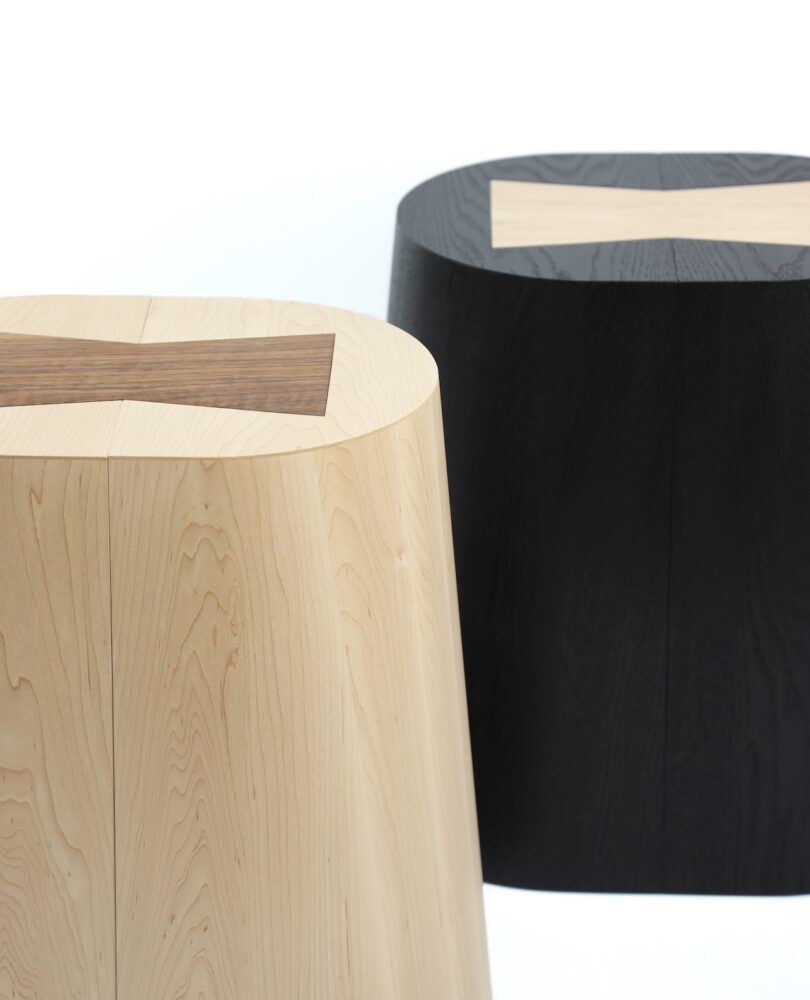 Two modern, cylindrical wooden stools with contrasting X-shaped inlays on their tops; one stool is light wood, the other is dark wood