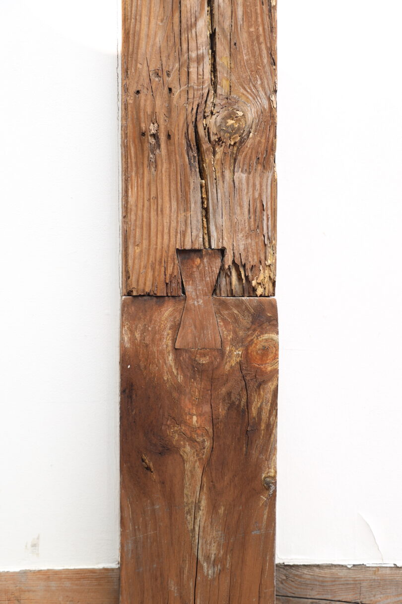 Two pieces of weathered wood joined vertically with a butterfly joint, against a white background and a wooden floor