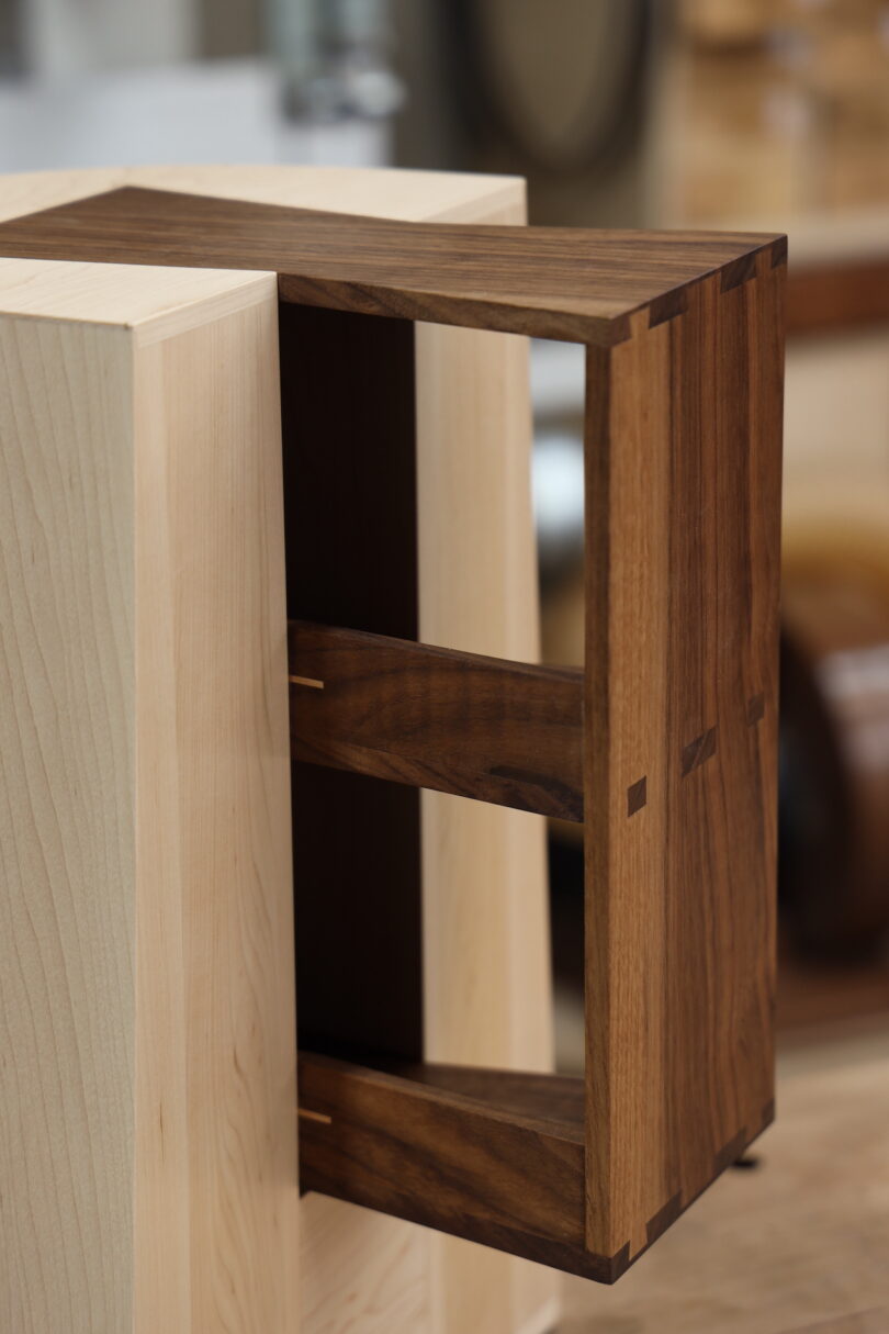 A wooden drawer with dovetail joints, made of dark wood, partially pulled out from a light wood cabinet